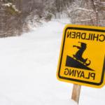 A bright yellow signsticks out of the snow. It has a graphic of a child on a sled and says "Children Playing."